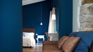 A modern hotel room with a brown sofa, a white table, and a bed with white linens. - Il Borgo B&B (Corato)