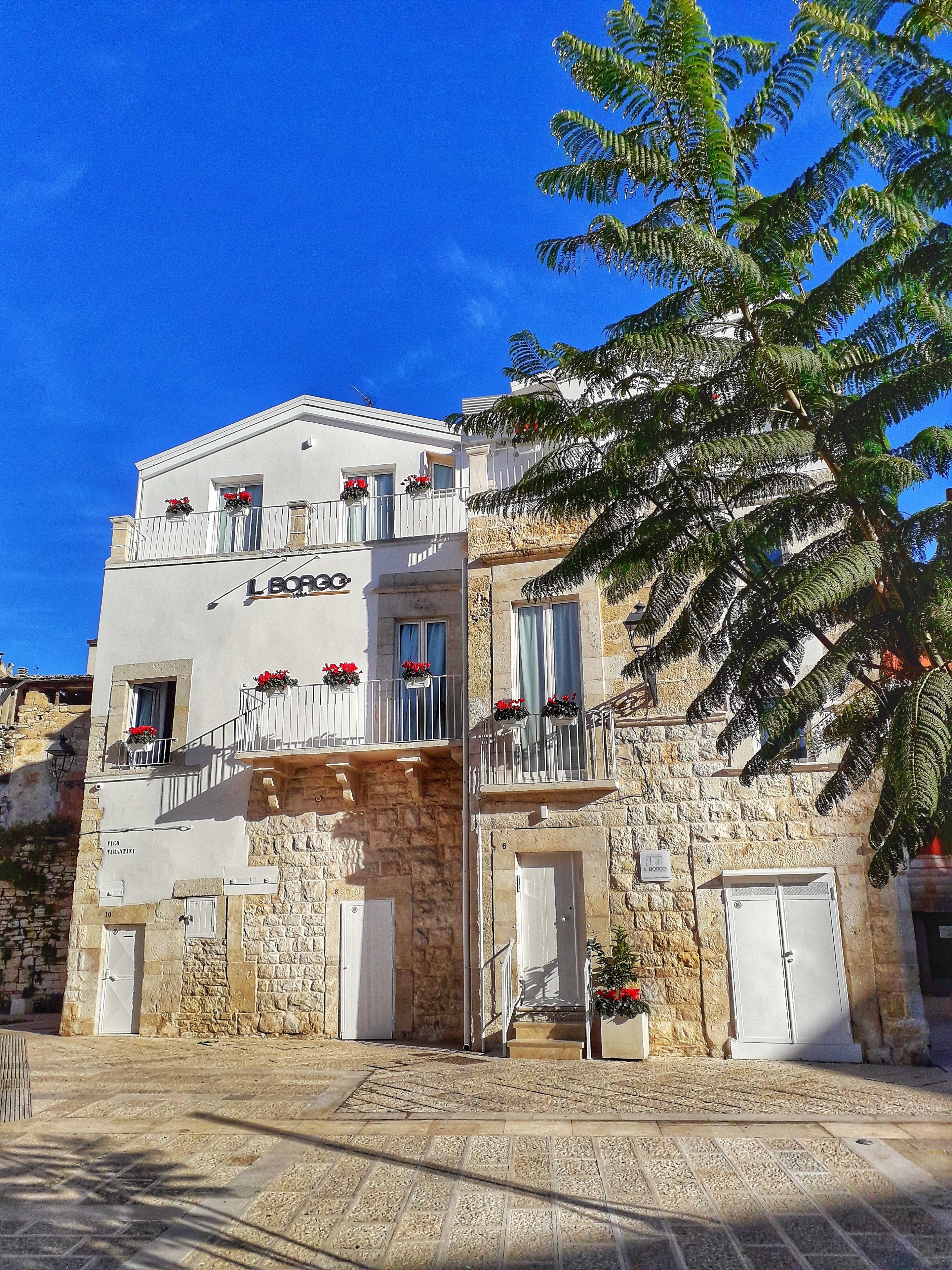 Un edificio de varios pisos con balcones, muros de piedra y jardineras.