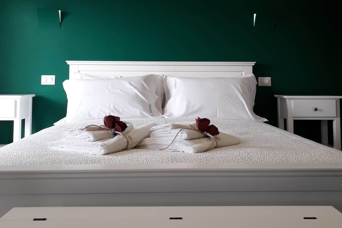 A neatly made bed with white linens and red roses, a white nightstand, and a white dresser.
