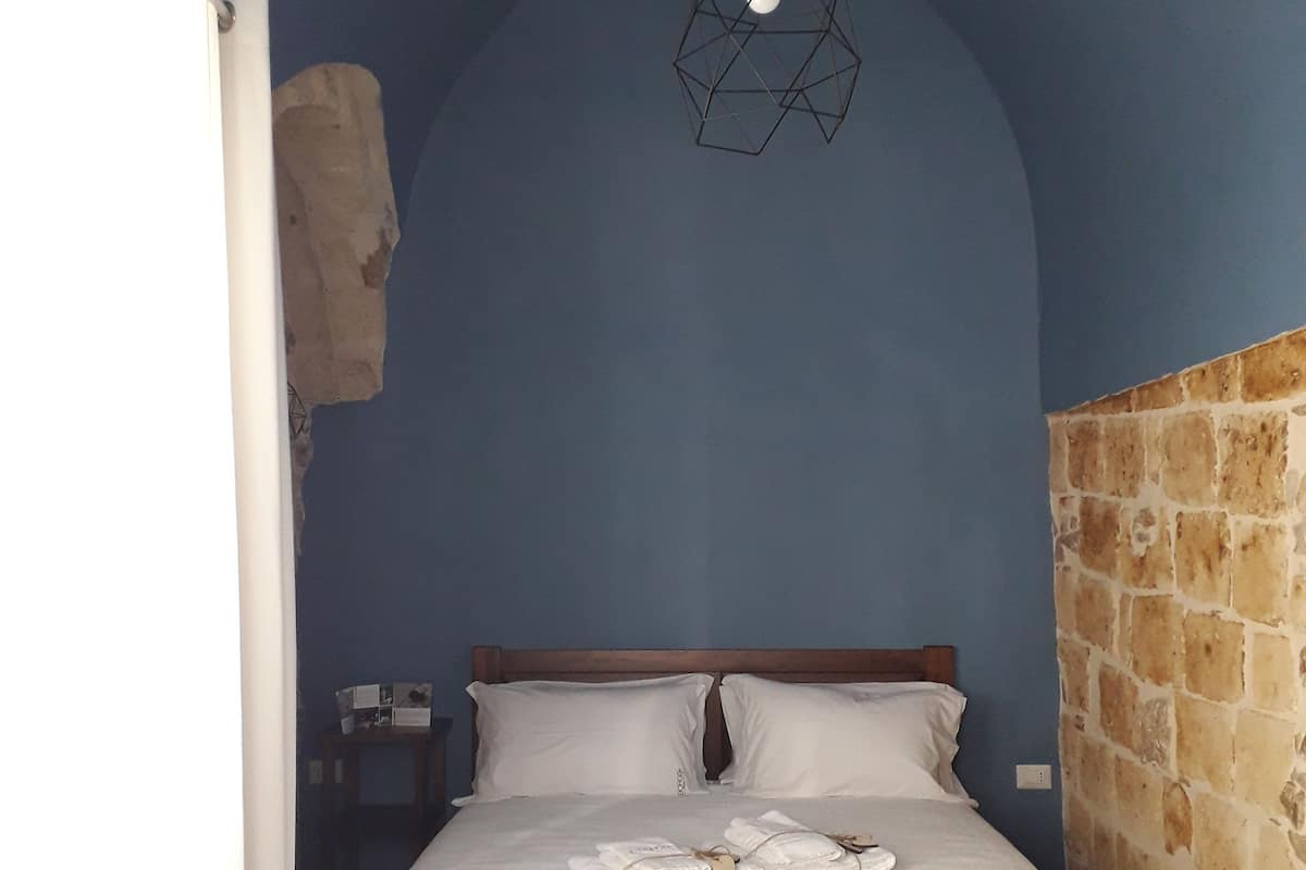 A neatly made bed with white linens, a wooden headboard, and two geometric pendant lights.