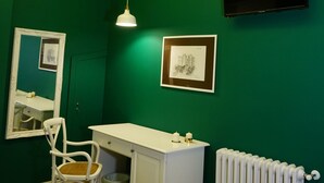 A room with a green wall, white ceiling, and a white desk with a chair. There is a framed picture on the wall and a radiator below. - Il Borgo B&B (Corato)