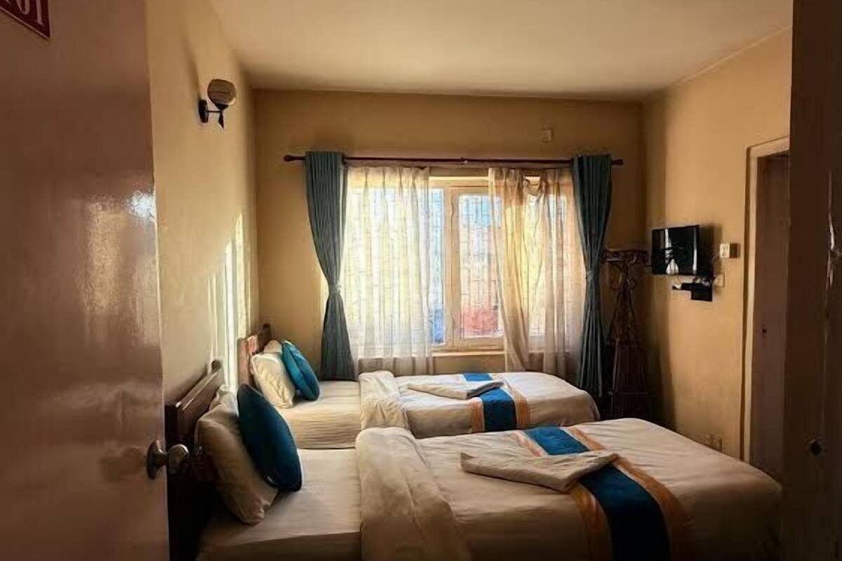 A room with two beds, a window with curtains, a door with a number sign, and a small table with a television.