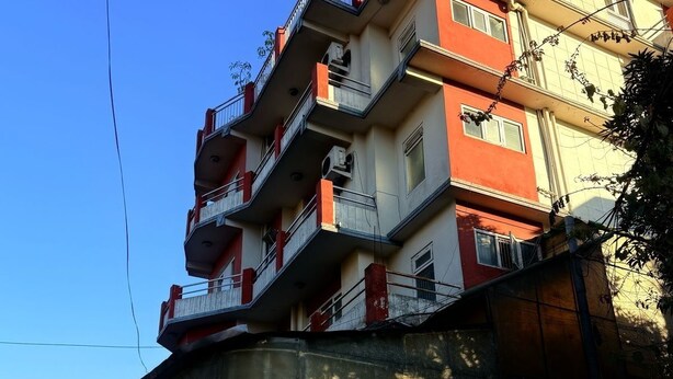 Um edifício de vários andares com varandas, uma placa com a inscrição '32 Peace Home' e uma placa de 'Proibido Estacionar'.