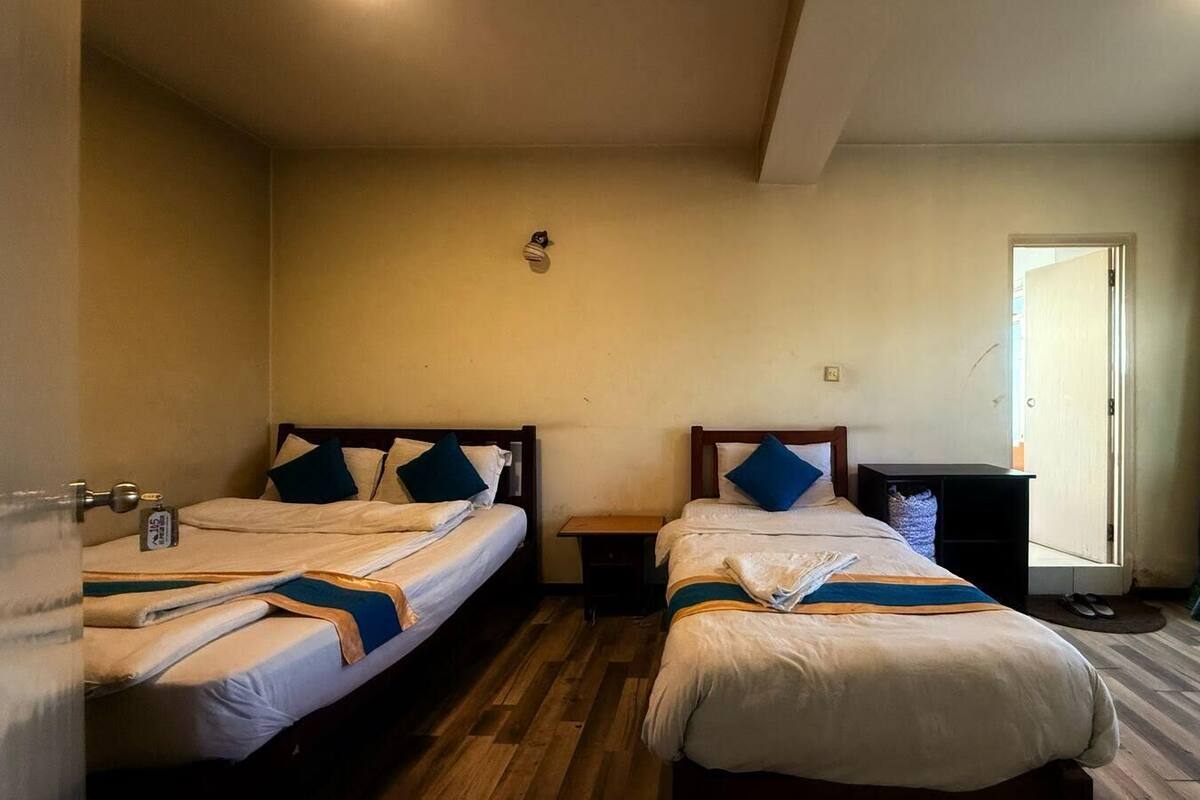 A hotel room with two single beds, wooden headboards, and a small bedside table.