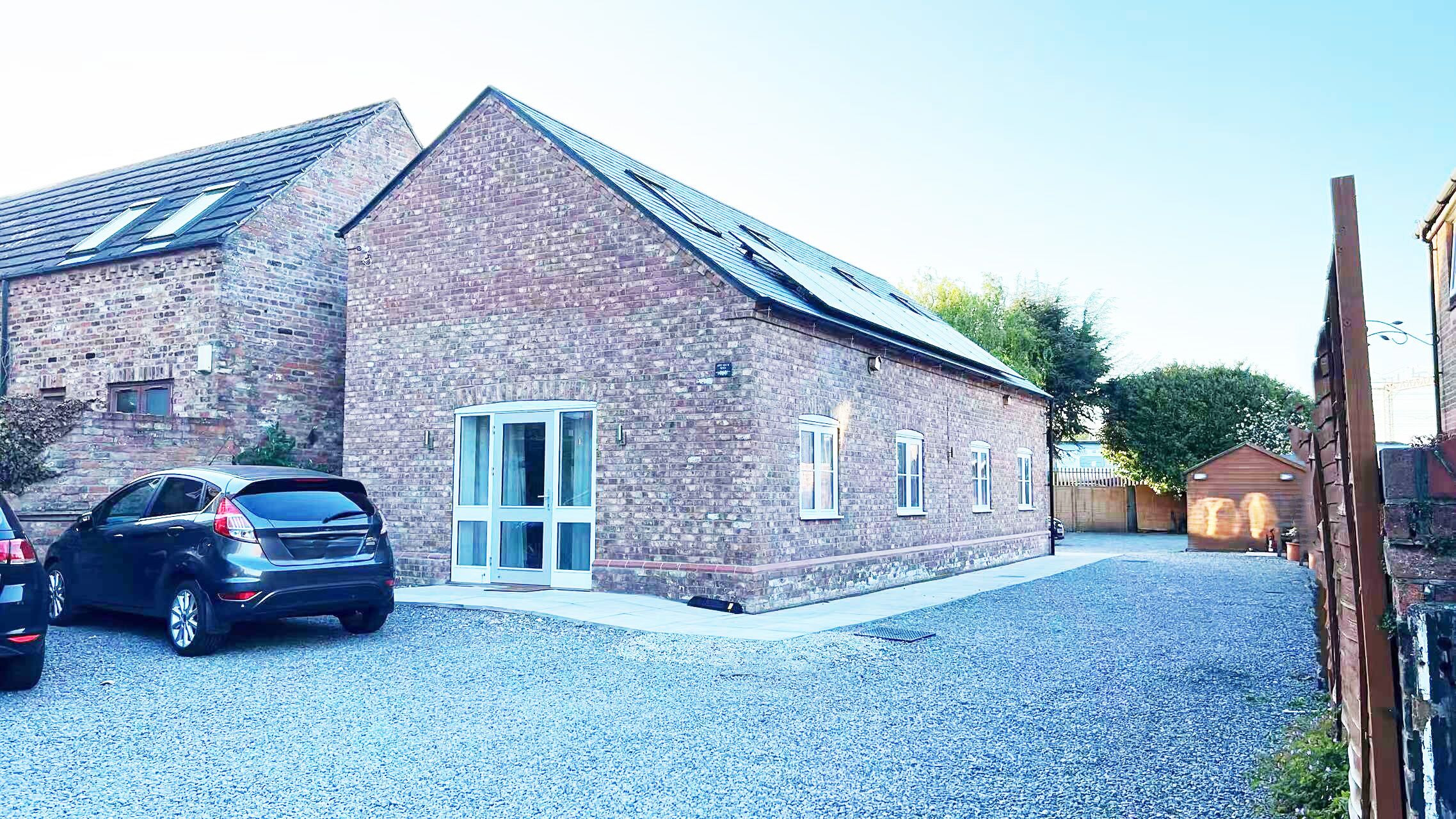 A brick building with a sloped roof, a garage door, and a gravel driveway.