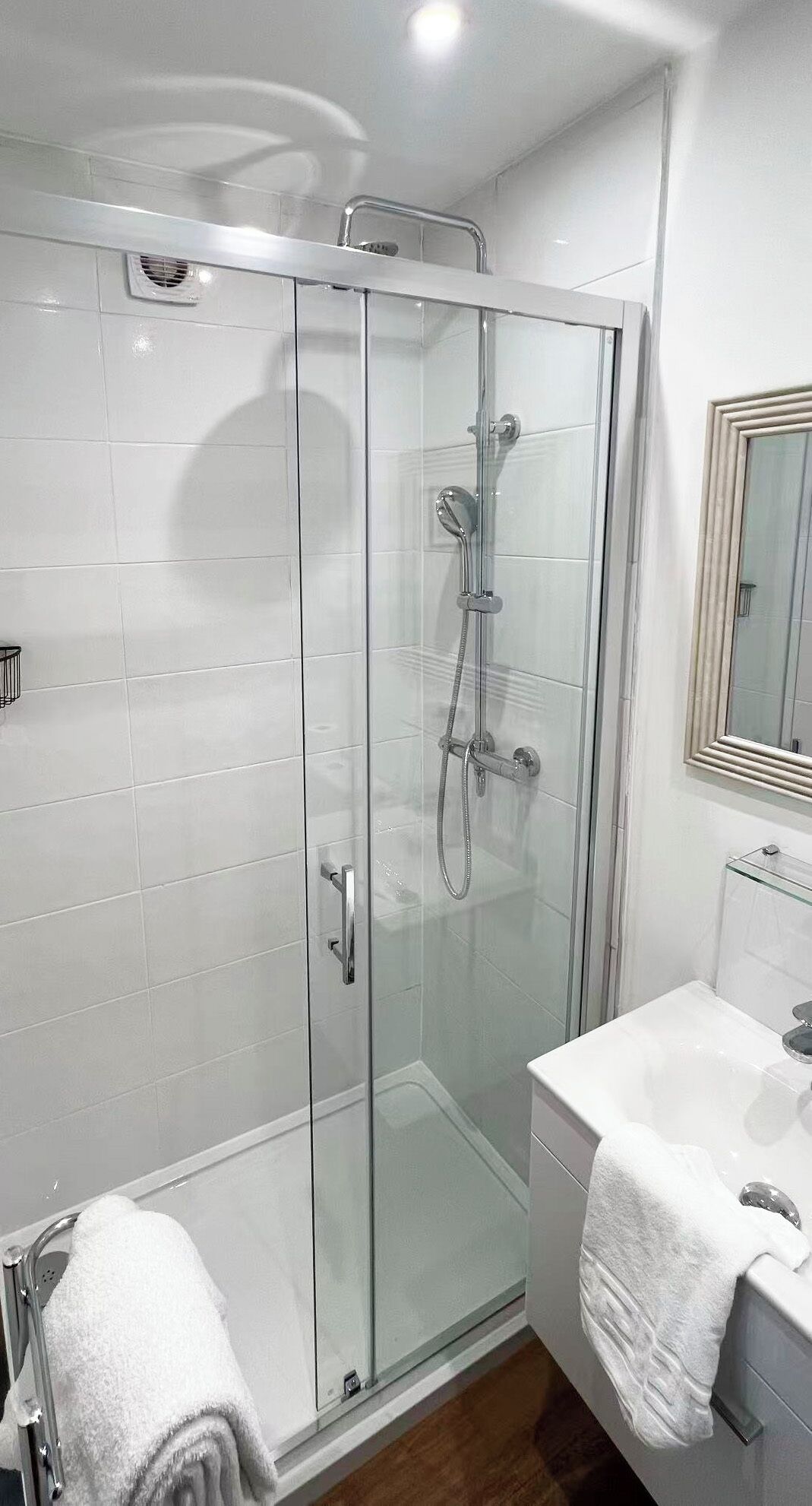 A modern bathroom with a glass-enclosed shower, a white sink, and a mirror above the sink.