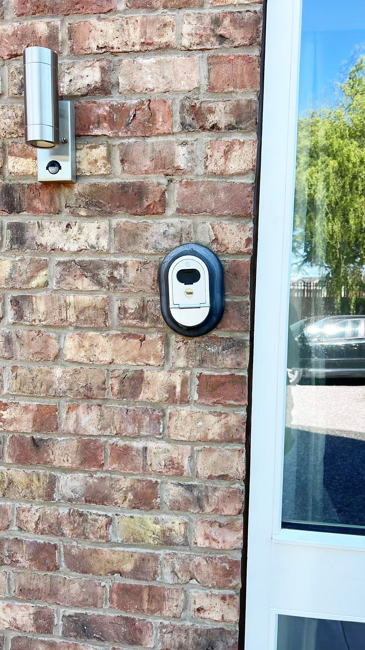 A brick wall with a Yale deadbolt lock and a metal intercom system.
