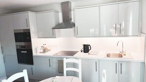 Una cocina compacta con armarios blancos, una estufa negra, un hervidor y un lavabo.