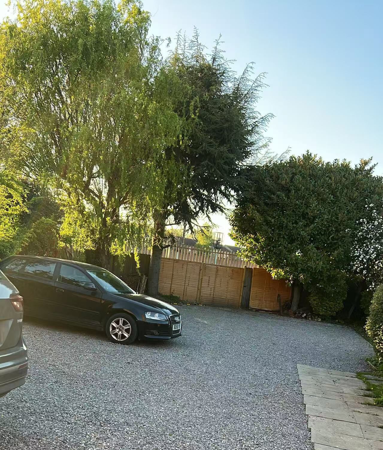Un camino de grava que conduce a un portón de madera, rodeado de árboles y un coche estacionado.