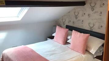 A bedroom with a sloped ceiling, a skylight, a bed with pink and white bedding, and a wall with deer head wallpaper.