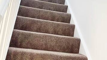 Eine Treppe mit Teppichbelag, die nach oben führt, mit weißen Wänden und einer Handläufe auf der linken Seite.