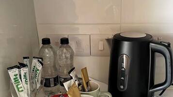 A kitchen counter with a coffee maker, two bottles, a tray with a mug, and food packets.