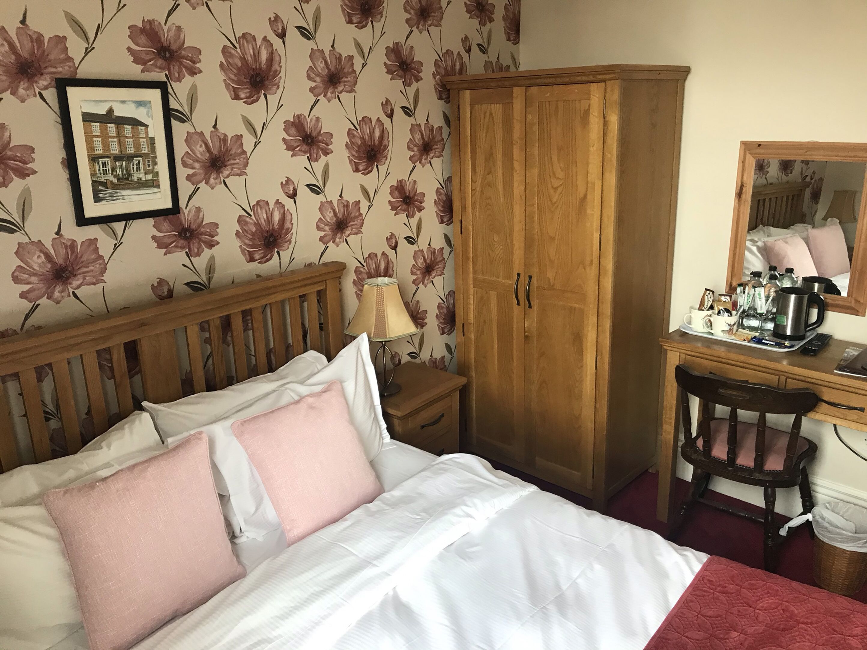A bedroom with a bed, wooden wardrobe, desk with chair, and a mirror.