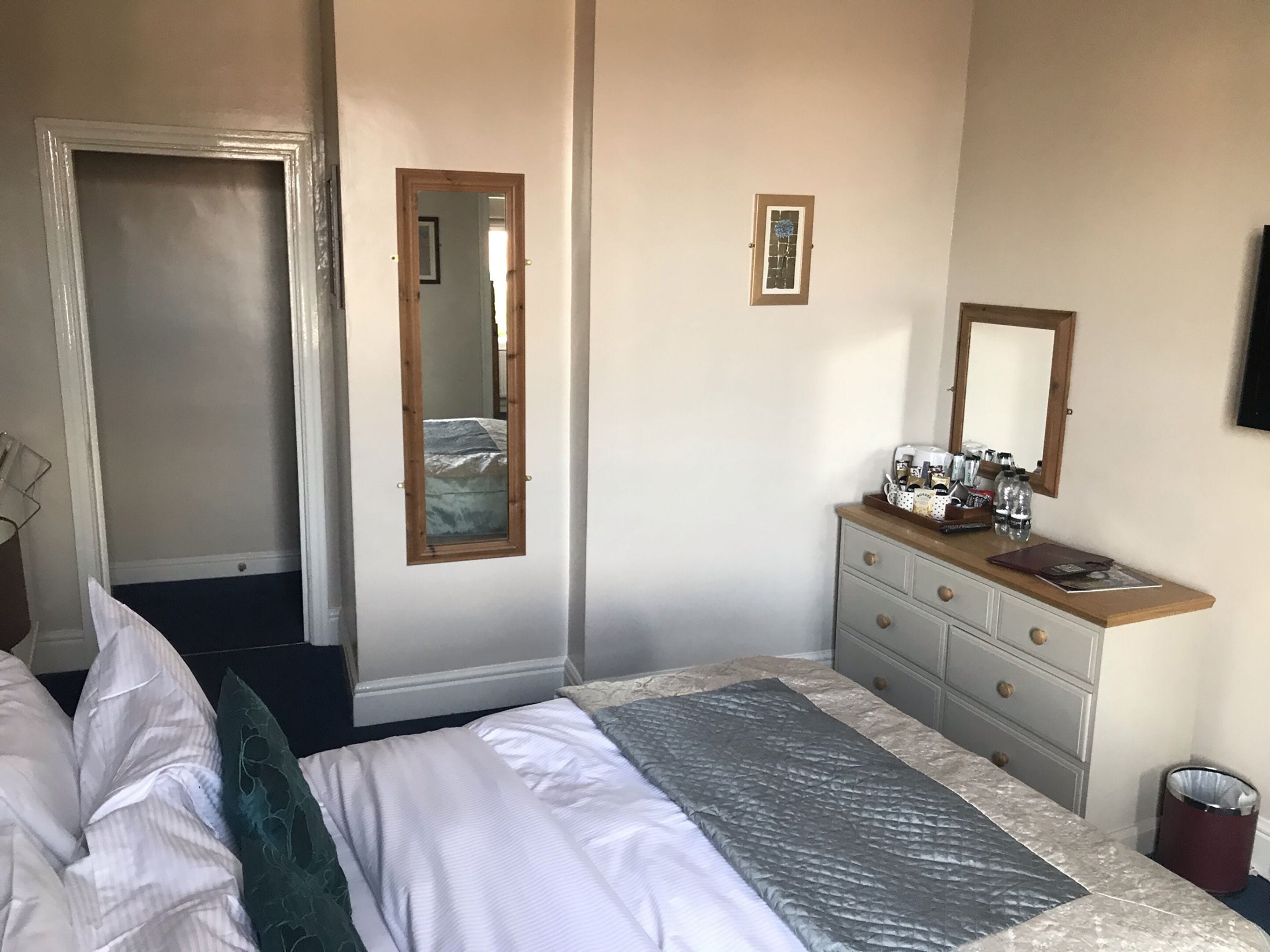 Une chambre à coucher avec un lit, une commode avec un miroir et une porte donnant sur une autre pièce.