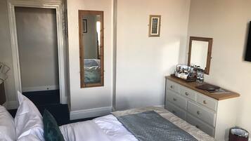 Une chambre à coucher avec un lit, une commode avec un miroir et une porte donnant sur une autre pièce.