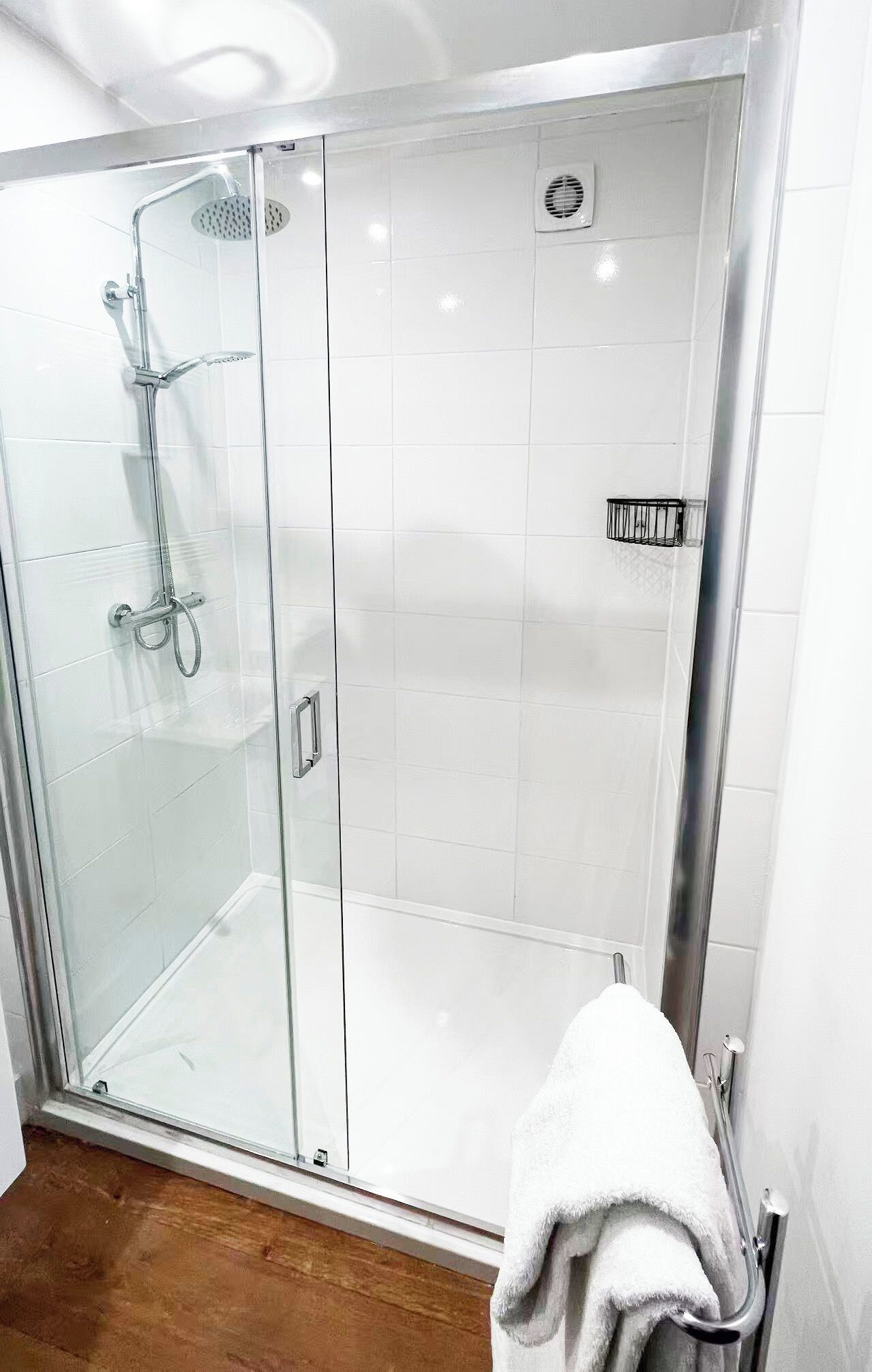 A glass-enclosed shower stall with a handheld showerhead, a handheld shower attachment, and a wall-mounted control panel.