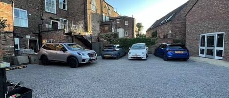 A parking area with four cars parked in front of brick buildings.