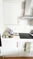 Una cocina con armarios blancos, una cocina por inducción negra y una pequeña encimera con alimentos y un cuaderno.