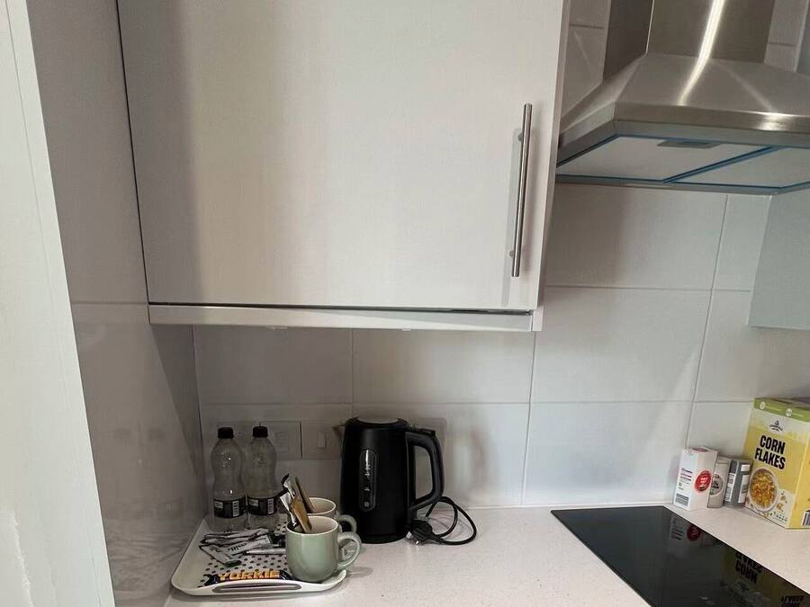 A kitchen with a stainless steel range hood, a kettle, a mug, a tray with utensils, and a box of corn flakes.