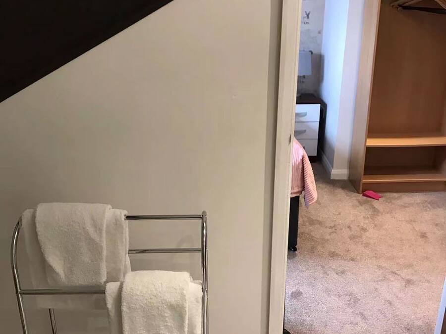 A room with a metal towel rack holding two white towels, a checkered floor, and a wooden closet with hangers.