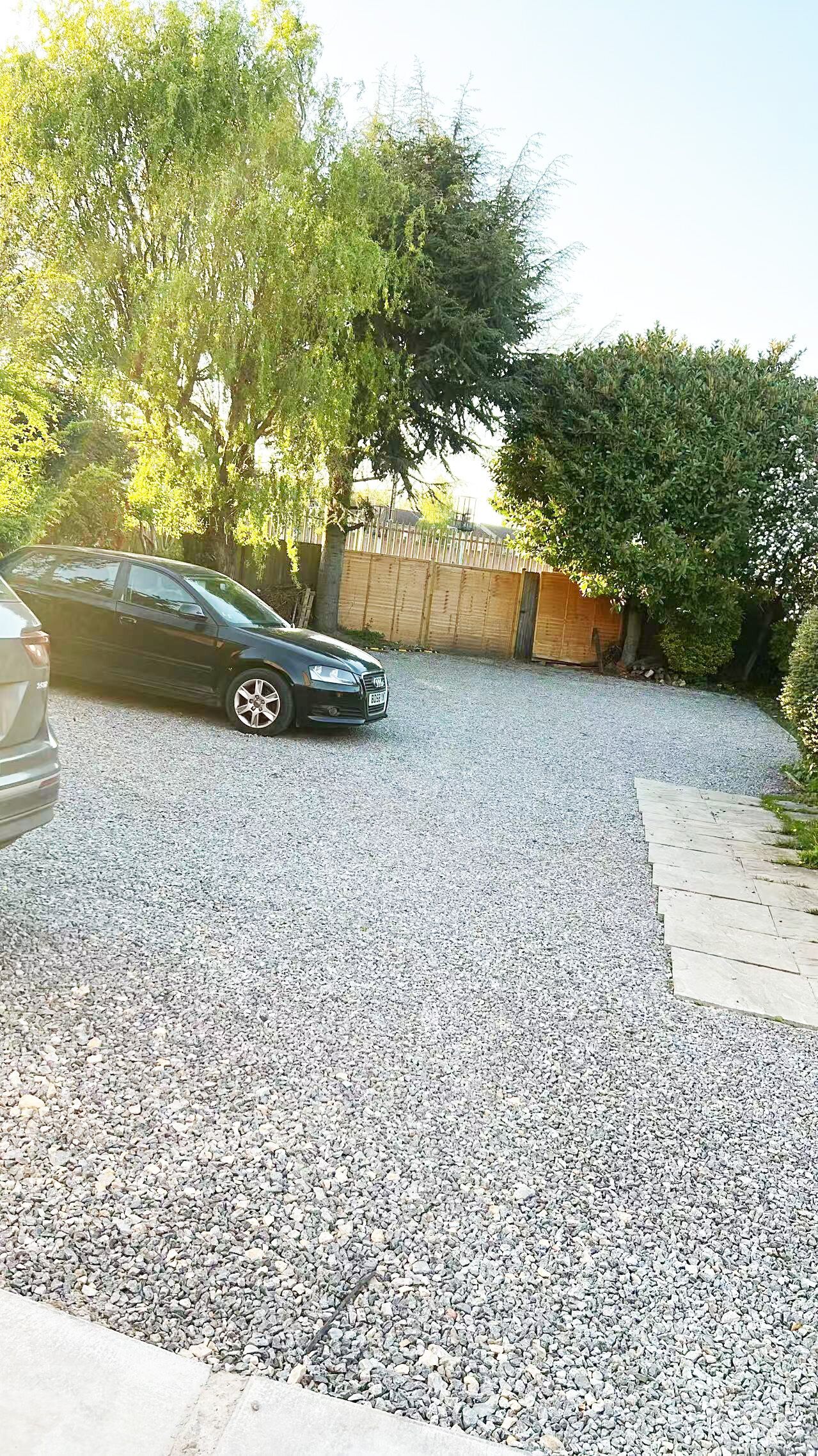 A gravel driveway with a parked car and a wooden fence.