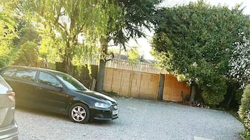 A gravel driveway with a parked car and a wooden fence.