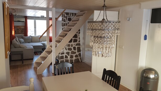 A modern kitchen with a white island, a chandelier, and a staircase with a stone wall. - Fantastic nature, hot tub, boat, sauna (Olofström / Gränum)