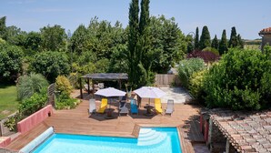 A swimming pool with wooden deck and lounge chairs, surrounded by lush greenery and tall trees. - Gîte Le Couvent    . (Cité de Carcassonne)