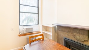 Una habitación con una mesa de comedor de madera, una ventana con aire acondicionado y una chimenea con azulejos decorativos.