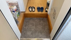 A narrow hallway with a wooden floor, a small carpeted area, and a pair of slippers on the floor. - Today's Bright and Cozy Room, Near Shibuya! (Setagaya)