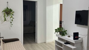 Ein modernes Wohnzimmer mit Deckenventilator, Fernseher, Sofa und einer kleinen, weißen Unterhaltungsecke.