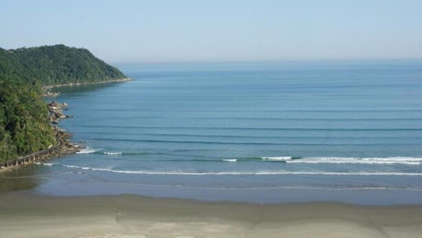 Eine Küstenlandschaft mit Strand, bewaldetem Hügel und ruhiger See.