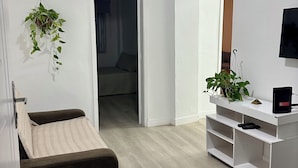 Ein modernes Wohnzimmer mit einer Couch, einem Fernseher, einer Pflanze und einer weißen Unterhaltungseinheit.