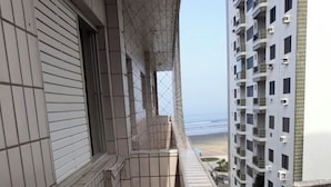 Ein schmaler Balkon mit Fliesenboden, Blick auf einen Strand und angrenzende Hochhäuser.