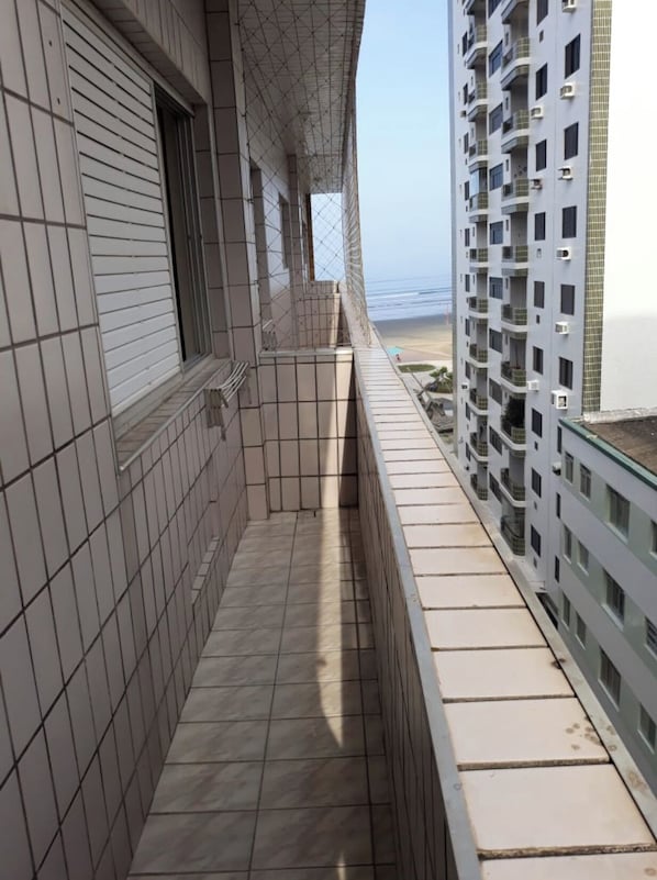 A narrow balcony with tiled flooring, overlooking a beach and adjacent high-rise buildings.