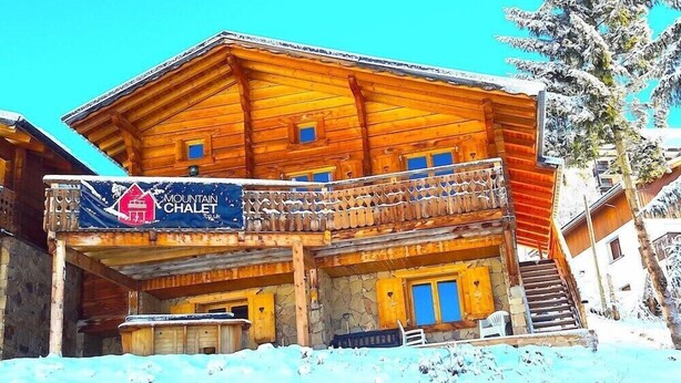 A wooden chalet with a balcony, a sign reading "Mountain Chalet," and a staircase leading to the entrance. - Mountain Chalet (Huez)