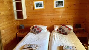 A wooden cabin room with two beds, each with a pillow and a small bedside table. - Mountain Chalet (Huez)