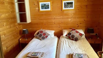 A wooden cabin room with two beds, each with a pillow and a small bedside table.