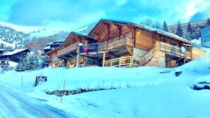 A wooden chalet with a balcony, surrounded by snow-covered hills.