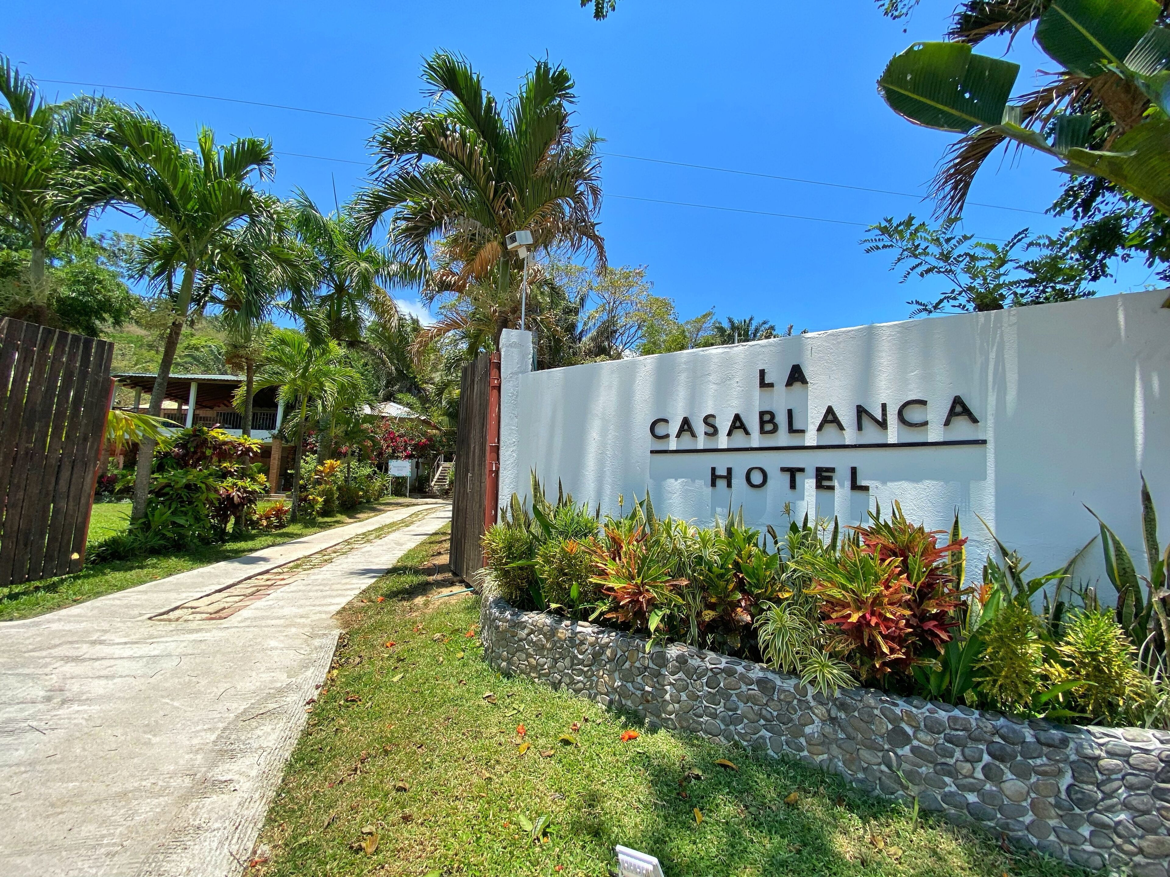 A sign for La Casablanca Hotel with a stone wall and tropical plants.