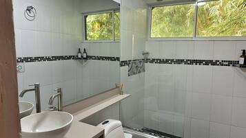 Un baño con lavamanos blanco, un espejo, inodoro y ducha.