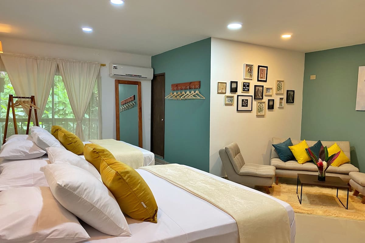 Habitación de hotel con dos camas, un sofá y una pared decorada con cuadros.