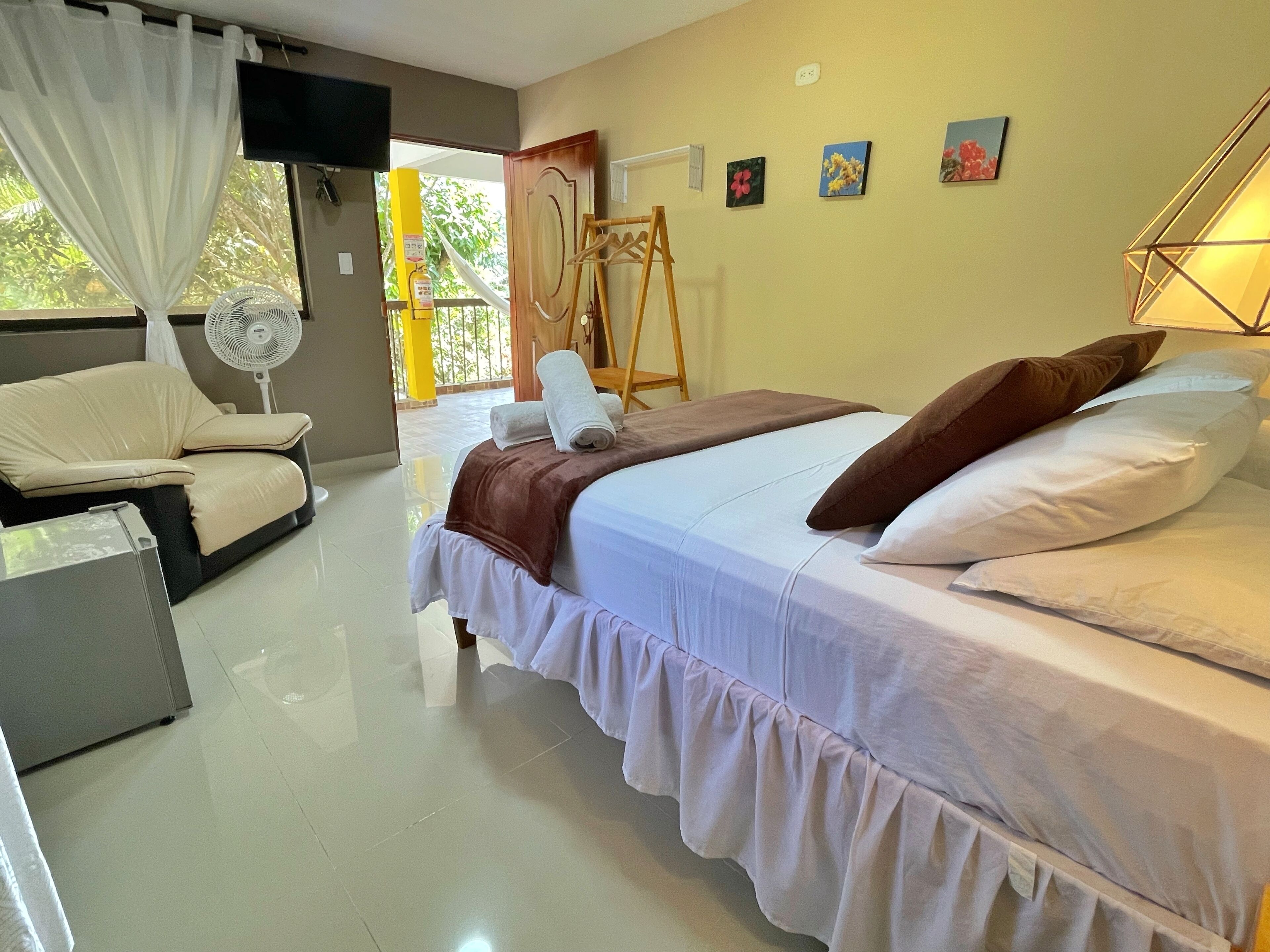 A bedroom with a bed, a chair, a fan, and artwork on the wall.