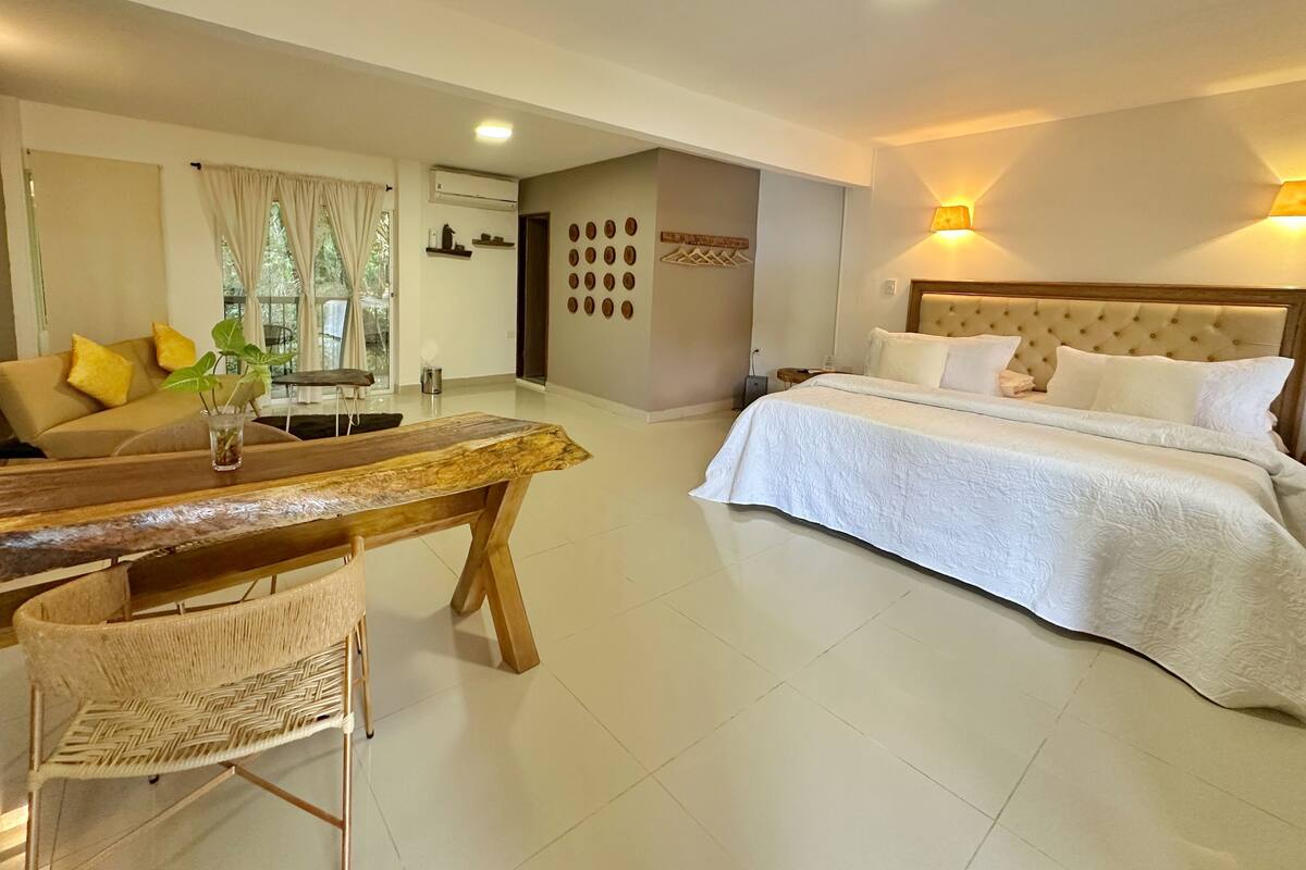 Una habitación de hotel con cama, una mesa de comedor con sillas, un sofá y una estantería de pared.