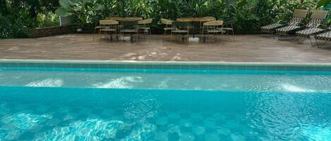 Piscina cristalina con cubierta de madera y zona de estar al aire libre.