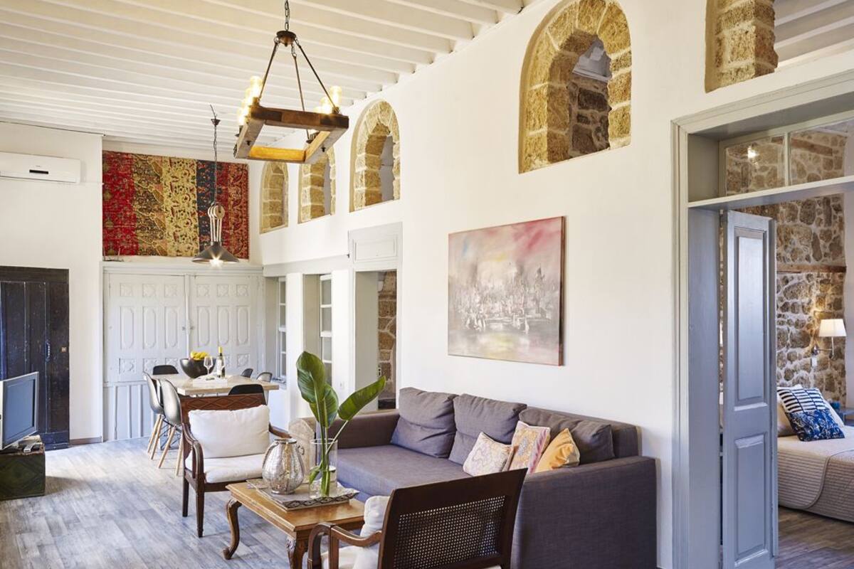 A spacious living area with a grey sofa, wooden chairs, a dining table, and a large window.