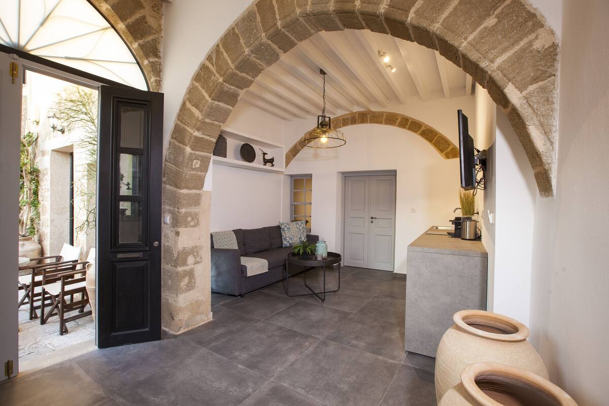 A cozy interior with a stone archway, a sofa with cushions, a small table, and a TV mounted on the wall.