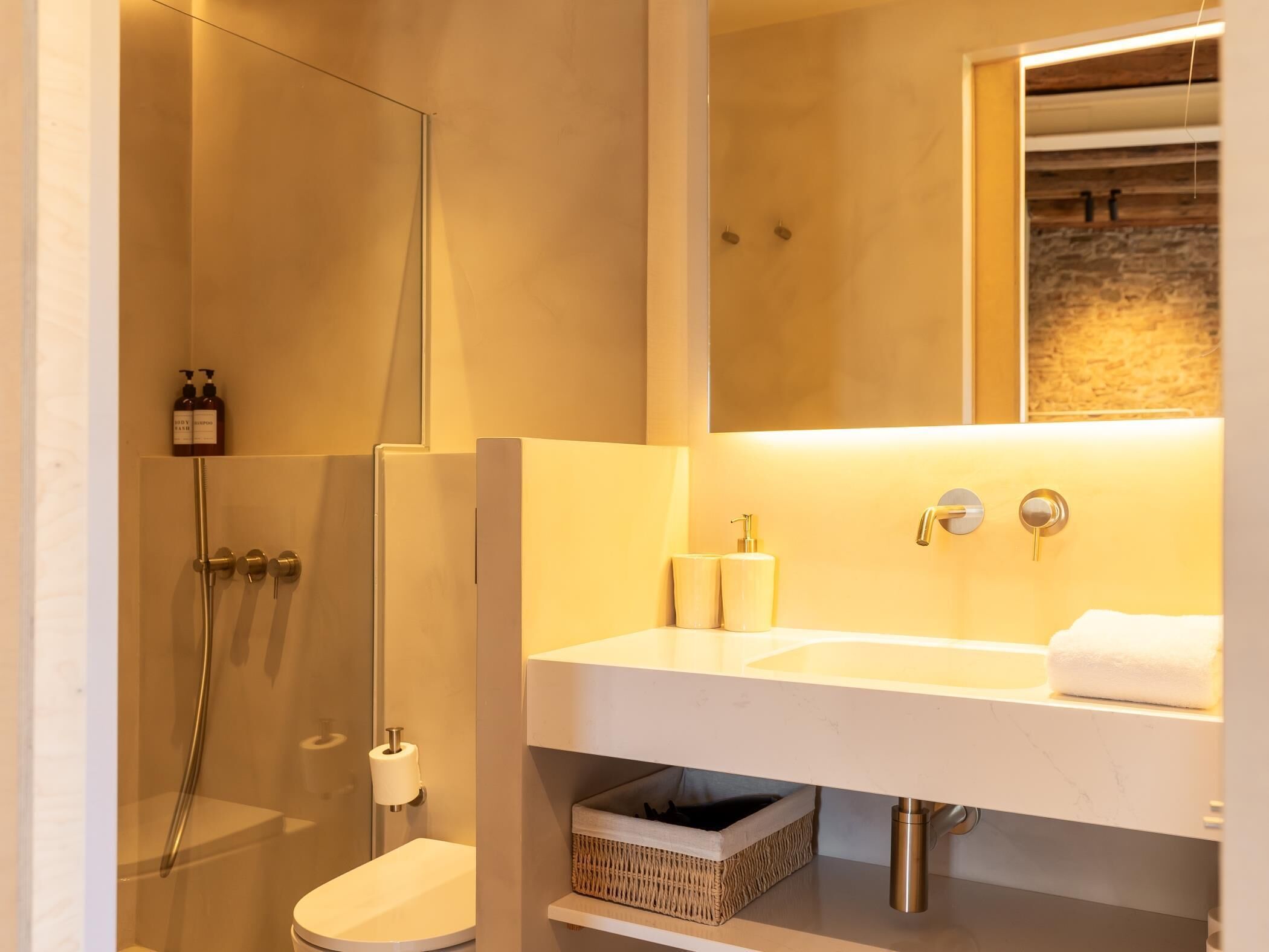 Een moderne badkamer met een douchecabine van glas, een witte wastafel met een marmeren aanrechtblad en een spiegel boven de wastafel.