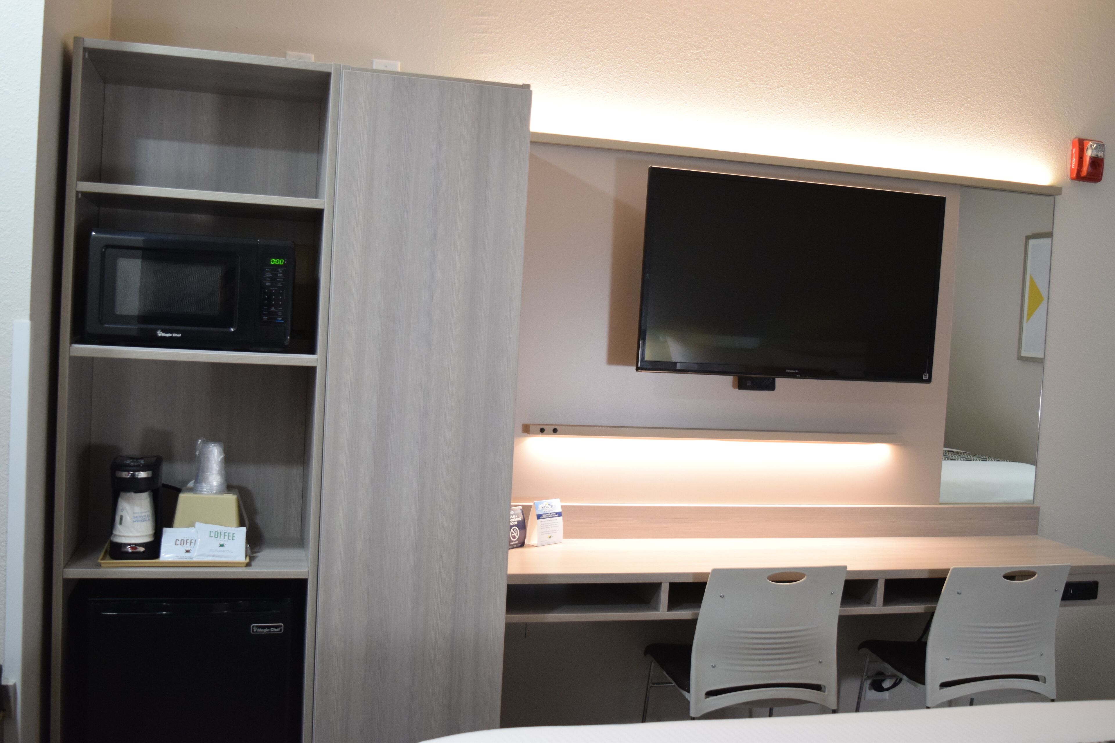 A hotel room with a microwave, coffee maker, and a flat-screen TV mounted on the wall.