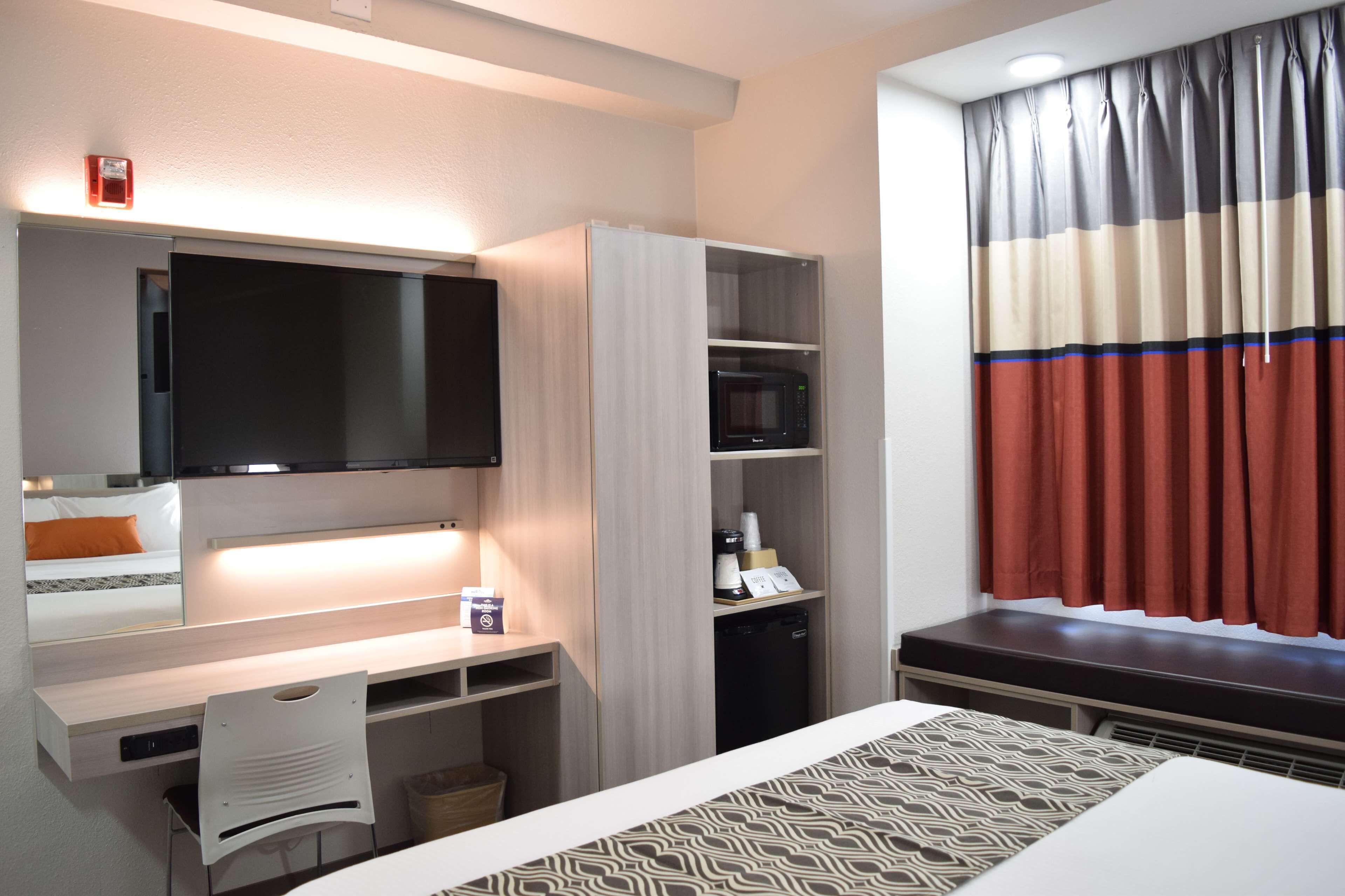 A hotel room with a bed, a desk with a chair, a television, a microwave, and a small refrigerator.